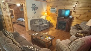 L’intérieur d’un chalet confortable en bois, avec un salon, une cheminée, un téléviseur et un coin repas.