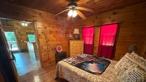 A wooden cabin bedroom with a bed, dresser, and a ceiling fan.