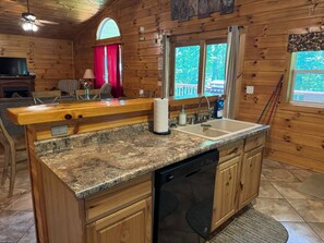 Une cuisine compacte dotée de meubles en bois, d’un plan de travail en granit, d’un lave-vaisselle et d’une fenêtre donnant sur un espace verdoyant.