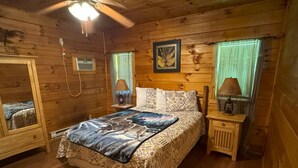 Une chambre dans une cabane en bois, avec un lit, des lampes de chevet, un miroir et un ventilateur de plafond.