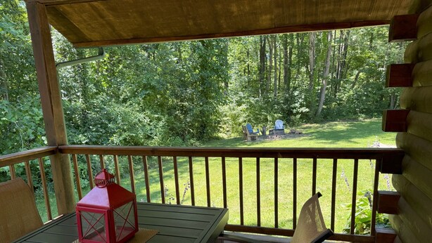 A covered outdoor seating area with a table and chairs, overlooking a grassy yard with trees.
