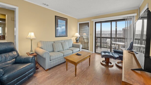A living room with a sofa, a coffee table, a TV, and a balcony with a view.