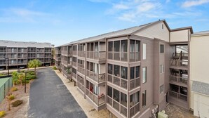A multi-story hotel with balconies, a parking area, and a clear sky.