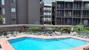 A rectangular pool with a wooden deck surrounding it, equipped with multiple lounge chairs and umbrellas.