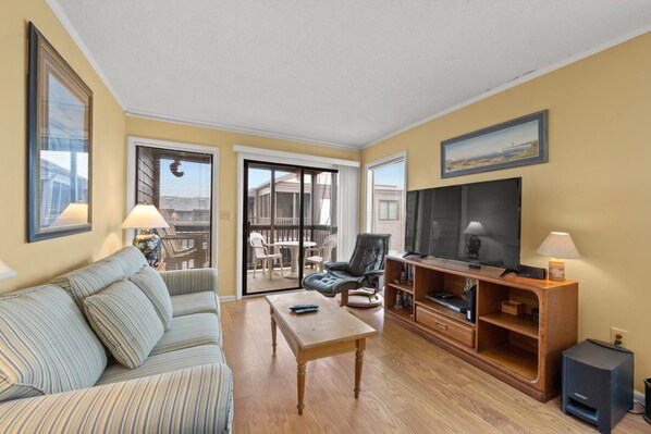 A living room with a sofa, a coffee table, a TV, and a fireplace. - Second row, three-bed, two-bath condo, fish décor, private porch | Tilghman Beach and Raquet - 354 (North Myrtle Beach)