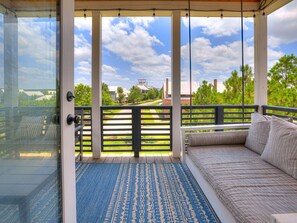 A covered balcony with a view of a building, a wooden bench, and a patterned rug.