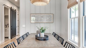 Ein Esszimmer mit einem langen Holztisch, schwarzen Stühlen, einer gewobenen Leuchte und einem geometrischen Wandbild.