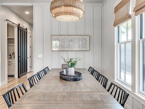 A dining room with a long wooden table, black chairs, a woven light fixture, and a geometric wall art piece.