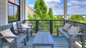 Eine überdachte Veranda mit Holzbanken und einem Tisch, Blick auf Bäume und Häuser, und bewölkter Himmel.