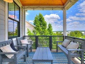 A covered porch with wooden benches and a table, a view of trees and houses, and a clear sky.