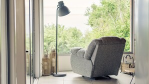 A modern living room with a grey sofa, a floor lamp, and a view of greenery through a large window. - Villa Mariense welcomes you in a landscape designed by nature! (Santa Barbara - Santa Maria - Azores Island)
