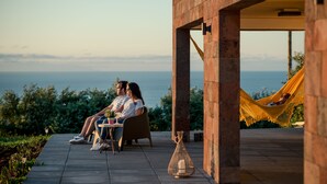 A couple sitting at an outdoor table with a view of the ocean. - Villa Mariense welcomes you in a landscape designed by nature! (Santa Barbara - Santa Maria - Azores Island)