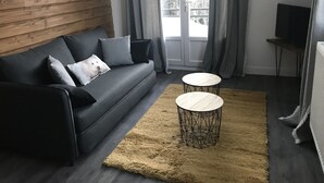 A modern living room with a dark grey sofa, two round wooden tables, a beige rug, and a wooden wall. - 4-6 Pers apartment in the heart of the Chartreuse at the foot of the ski slopes (Sarcenas)