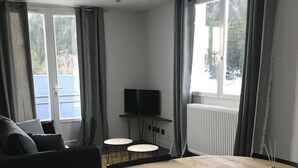 A modern living room with a round wooden table, black chairs, a sofa, and a TV on a stand. - 4-6 Pers apartment in the heart of the Chartreuse at the foot of the ski slopes (Sarcenas)