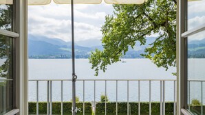 A balcony with a view of a lake and mountains, featuring a wooden deck and a beige umbrella. - Exclusive with lake view, free parking space and high-quality furnishings (Tegernsee)