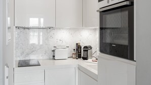 A modern kitchen with white cabinetry, a built-in oven, and a countertop with a coffee maker and toaster. - Exclusive with lake view, free parking space and high-quality furnishings (Tegernsee)
