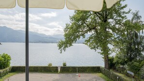 A lakeside view with a large umbrella, a tree, and a signpost. - Exclusive with lake view, free parking space and high-quality furnishings (Tegernsee)