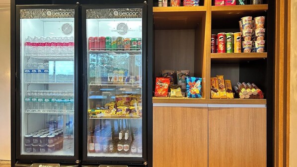 Una máquina expendedora con diversas bebidas y aperitivos, y un estante con productos envasados.