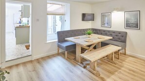 Uma sala de estar moderna com um sofá cinzento, mesa de jantar de madeira e uma pequena planta em vaso.