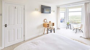 Quarto de hotel com uma cama grande, uma mesa de cabeceira de madeira com uma cadeira, uma televisão na parede e uma varanda com vista para a paisagem.