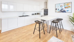 A modern kitchen with white cabinetry, a central island with bar stools, and a large abstract painting on the wall.