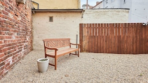 Un banco de madera en un patio con suelo de grava, una pared de ladrillo y una valla de madera.