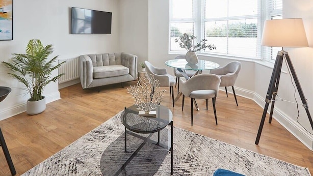 A modern living room with a sofa, a glass coffee table, and a dining area with chairs.