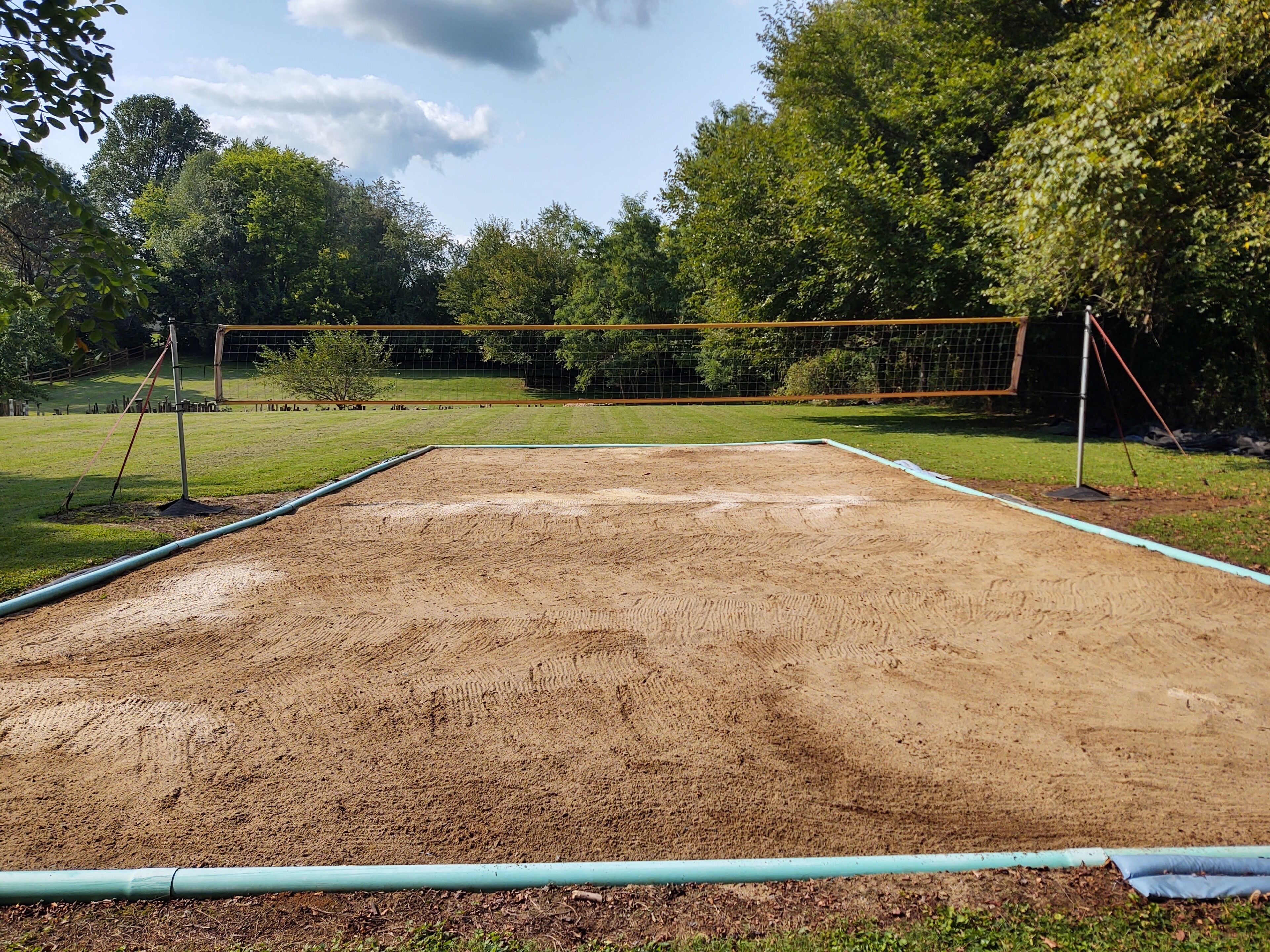 Uma quadra de voleibol com rede, rodeada por árvores e grama.