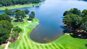 Vista aérea de un campo de golf con un lago grande, rodeado de árboles densos y césped cuidado.