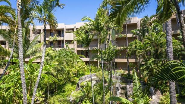 A hotel with multiple balconies, lush tropical vegetation, and a rocky water feature.