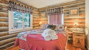 Un dormitorio de estilo cabaña de troncos con un ventanal grande, una colcha acolchada y una mesita de noche con una lámpara.