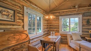 Interior de una cabaña de troncos con una mesa de comedor, sillas, un sofá y una chimenea.