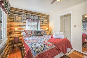 A bedroom with a wooden log wall, a bed with a quilt, two bedside lamps, and a window with curtains. - Wine Gazebo Pikes Peak Mountain Log Cabin (Cascade-Chipita Park)