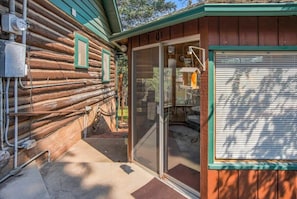 Une cabane en rondins avec une porte d’entrée en verre, un petit porche et une fenêtre avec des stores.