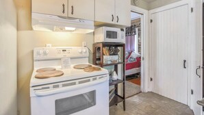 Una cocina compacta con armarios blancos, estufa y microondas.
