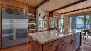 A modern kitchen with a large island, stainless steel appliances, wooden cabinetry, and a view of the outdoors.