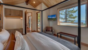 A bedroom with a large bed, a chair, a small table, and a window with a view of trees and mountains.
