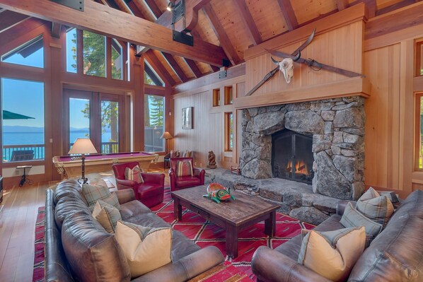 A cozy cabin interior with a stone fireplace, leather sofas, and a pool table.