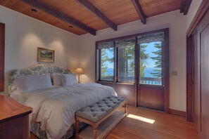 A bedroom with a large bed, a bedside table, a lamp, and a window with a view of the ocean. - Sunrise by Sunnyside - Lakefront - TLUXP (Tahoe City)
