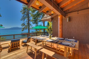 A wooden deck with a table set for dining, overlooking a lake with mountains in the distance. - Sunrise by Sunnyside - Lakefront - TLUXP (Tahoe City)