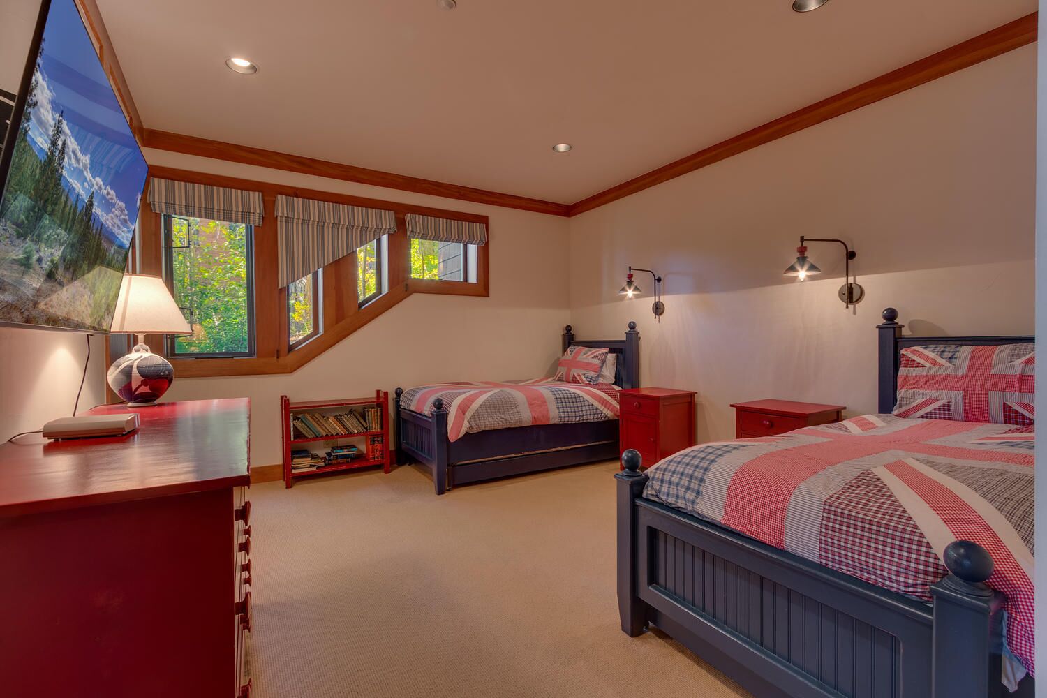 A bedroom with two beds, a desk, a bookshelf, and a large window with curtains.