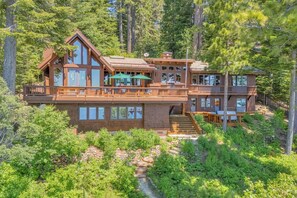 A two-story wooden cabin with a balcony, surrounded by dense forest. - Sunrise by Sunnyside - Lakefront - TLUXP (Tahoe City)