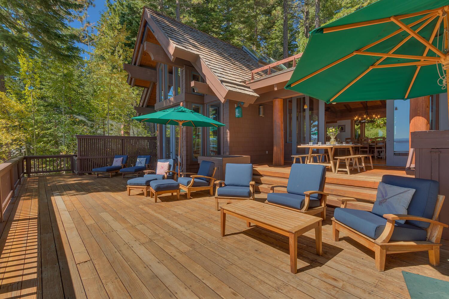 A wooden deck with outdoor seating, a covered area, and a view of the surrounding trees.