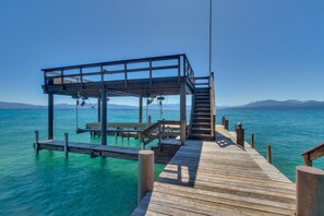 A wooden pier leading to a covered structure with a staircase, overlooking a calm body of water and distant mountains. - Sunrise by Sunnyside - Lakefront - TLUXP (Tahoe City)