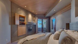 Een slaapkamer met een groot bed, een open haard, een televisie en een schuifdeur naar een buitenruimte.