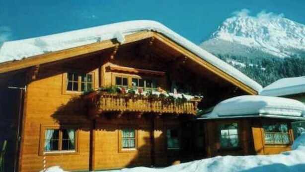 Una cabaña de madera con balcón, rodeada de nieve y montañas.