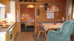 Una cocina acogedora con paredes de madera, una mesa de comedor con mantel a cuadros y una silla de mimbre.