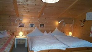 Un dormitorio de cabaña de madera con una cama, dos mesitas de noche con lámparas y un pequeño estante en la pared.