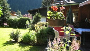 Un jardín con una maceta colgante, una terraza de madera y un edificio con tejado inclinado.