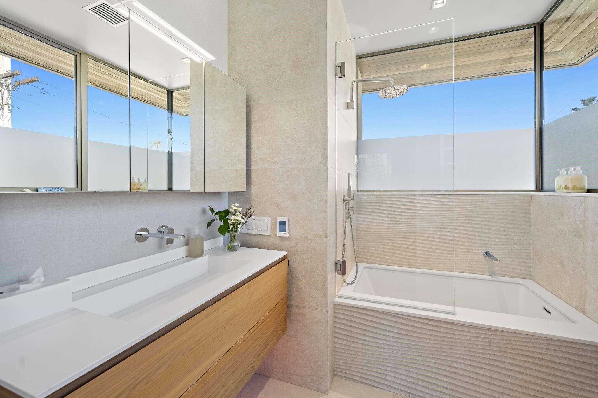 Une salle de bain moderne avec un grand miroir, deux vasques, un meuble-lavabo en bois, une douche à parois de verre et une baignoire.